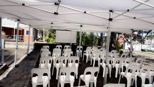 projector screen with plastic chairs set up under a pop up marquee